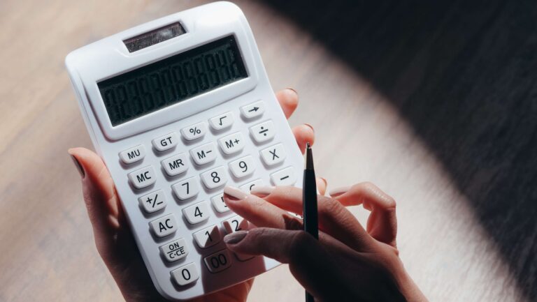 Mano de una persona sostiene una calculadora y un lápiz mientras calcula una cifra.