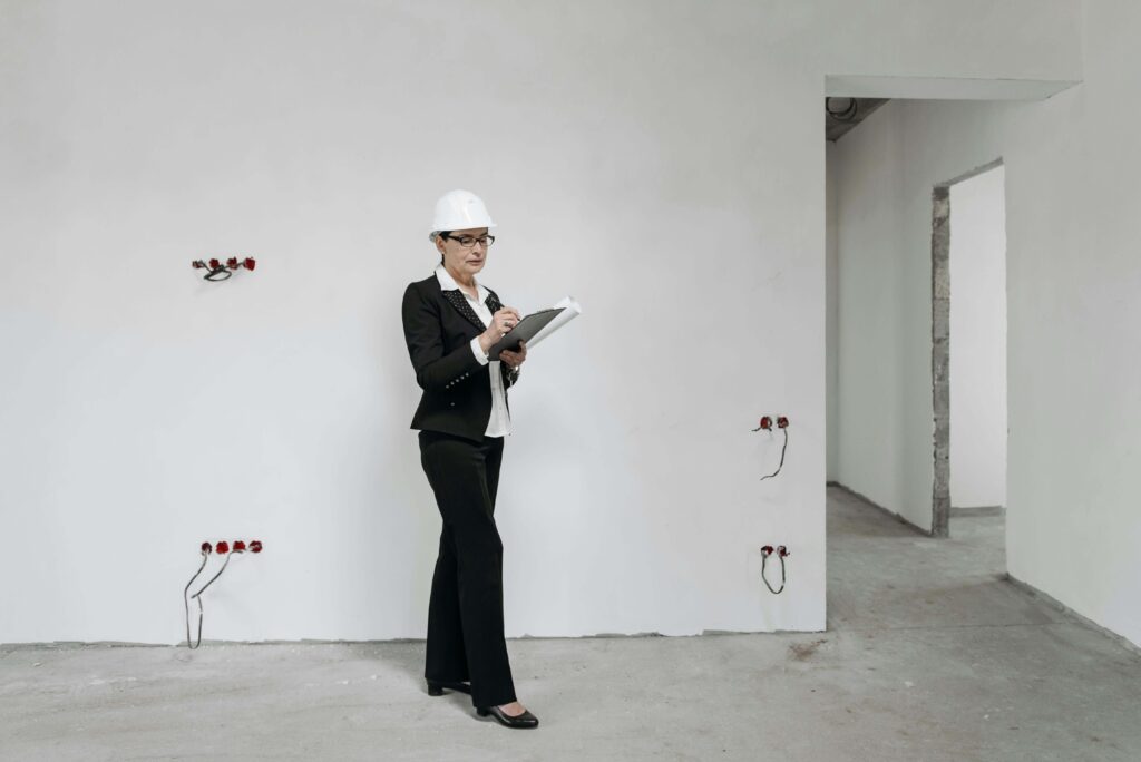 Una mujer vestida con traje negro y casco blanco revisa una habitación aún no terminada.